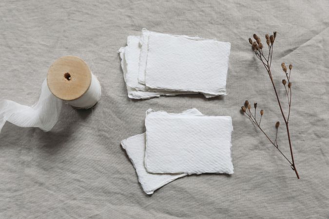 Winter wedding stationery still life concept. Pile, set of blank cotton paper business, place cards. Invitations mockups. Dry flower, seeds, chiffon ribbon. Beige linen table cloth background. Sparse flat lay, top view.