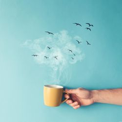 Coffee cup with steam, clouds and birds on blue background