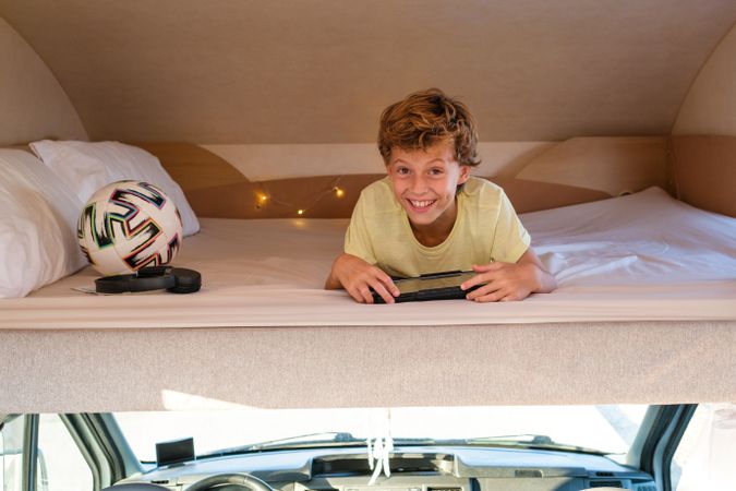 Cheerful boy with tablet resting on caravan bed