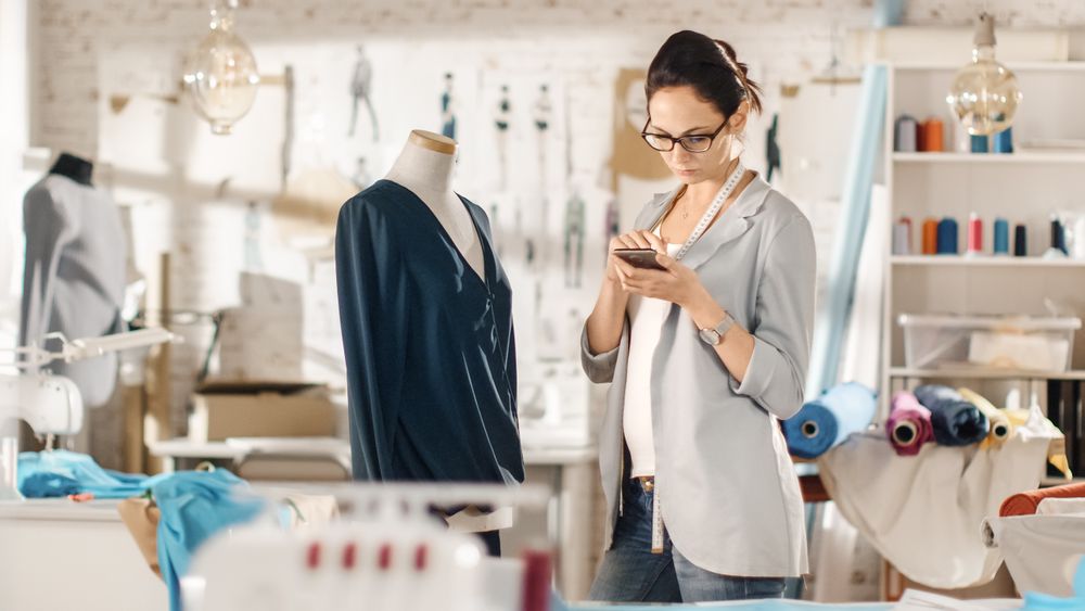 Woman fashion, designer,  Working with Tailoring Mannequin, Adjusting Blouse, Using Smartphone.
