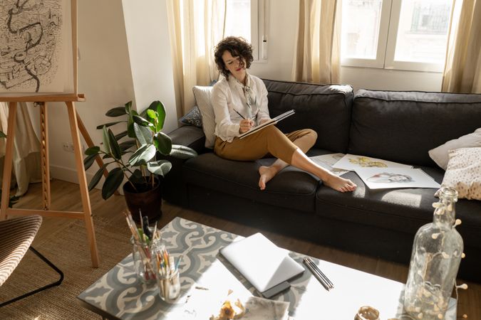 Woman writing on paper on sofa in room