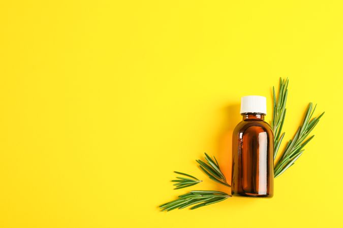 Flat lay composition with rosemary oil and leaves on yellow background, space for text