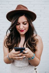 Woman in hat smiling browsing smartphone