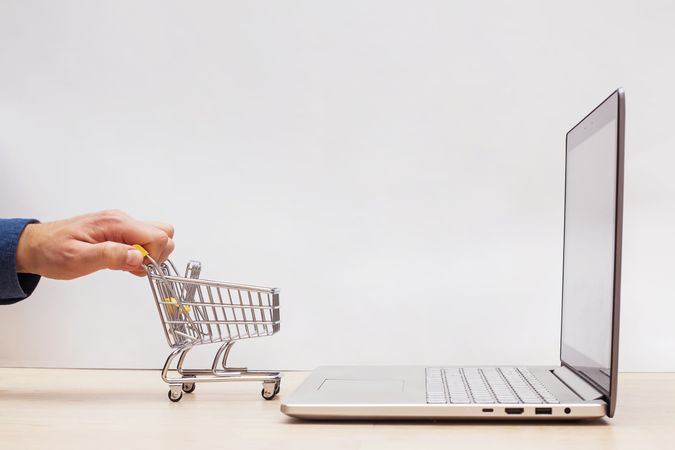 Person Using Mini Shopping Cart to Access Online Shopping via a Laptop
