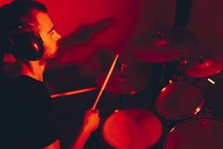 Man with drumsticks playing on drums in redness