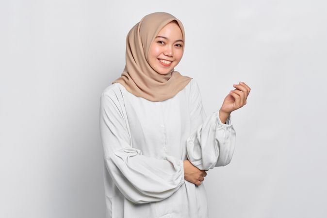 Smiling Asian female in headscarf with hand up