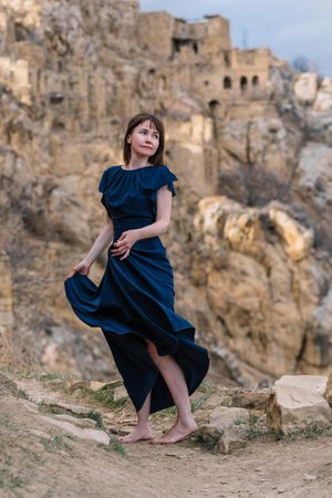 Woman in long blue dress standing near abandoned village during daytime