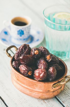 Copper bowl of dates with espresso and water in background