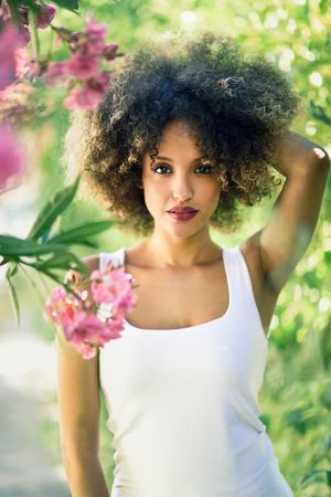 Portrait of beautiful Black woman with afro hairstyle in park with one arm up to her head, vertical