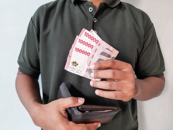 a man holding a wallet and Indonesian rupiah banknotes with a nominal value of one hundred thousand rupiah