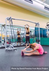 Woman pink stretching on gym floor as other woman works out upper body bxXGZb