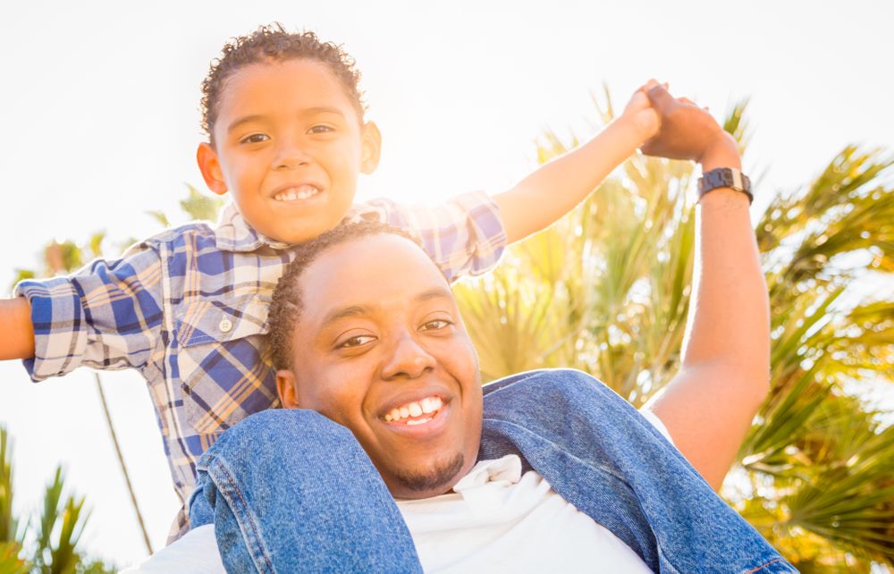 Son Piggybacking On Father's Back Outdoors Together On Sunny Day