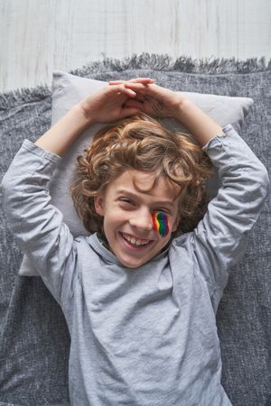 Cheerful boy with rainbow drawing lying on pillow