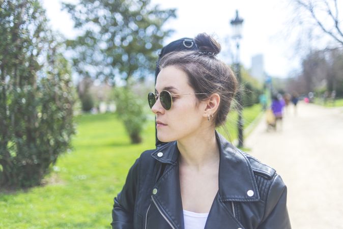 Front view of a young smiling hipster woman walking in a park in sunny day while carrying a guitar on back and looking away