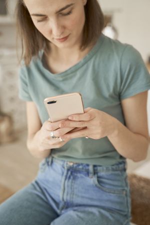 Relaxed women sitting on washing machine and browsing smartphone