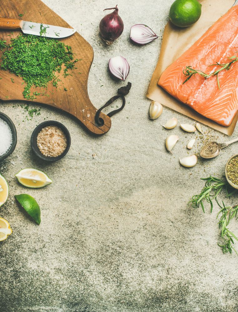 Salted salmon fillet with fresh herbs, limes, onions, bread board, copy space