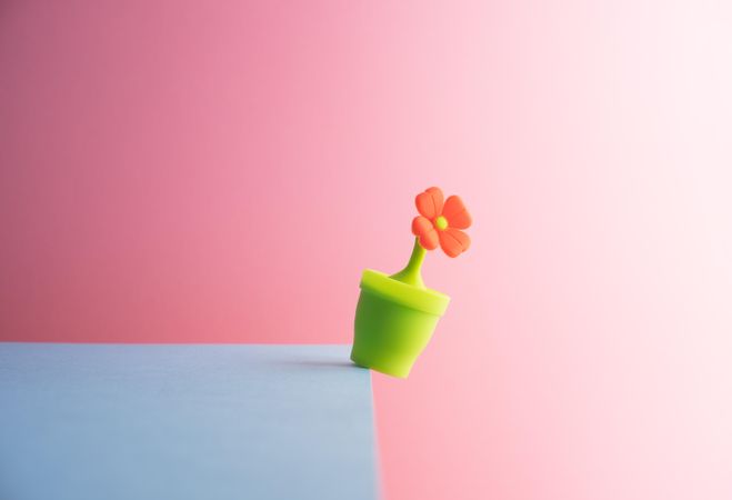 Plastic flower in pot about to fall over the edge