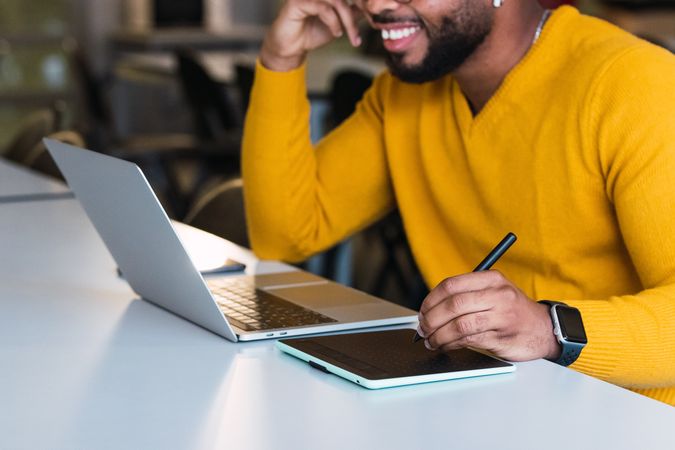 Anonymous smiling Black man working on laptop with tablet