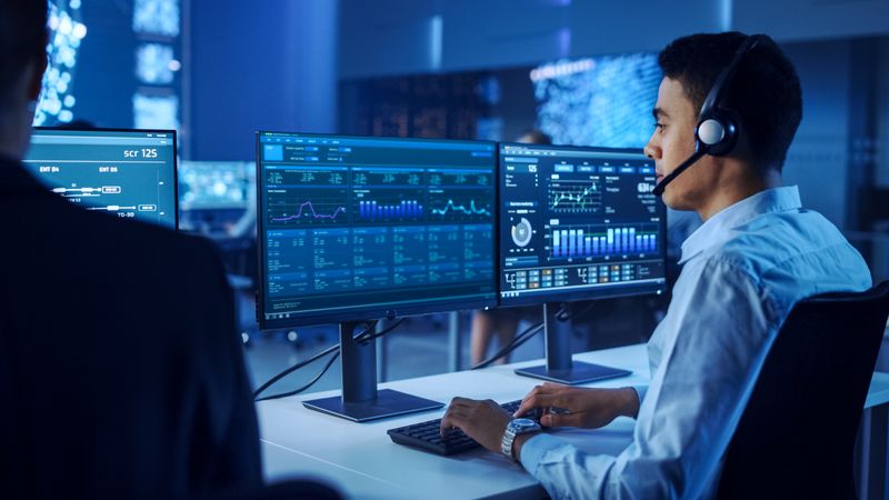 Focused Professional Analyzes Complex Data on Dual Monitors in a High-tech Control Room, Enhancing Cybersecurity and Operational Efficiency. the Environment Fosters Innovation and Strategic Decision-making.