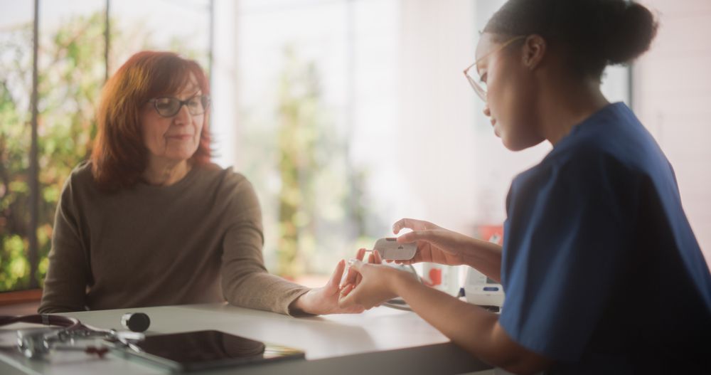 Black Healthcare Nurse Taking a Blood Sample to Measure Sugar Levels for a Mature Patient.