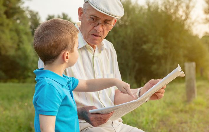 Older man with boy reading a newspaper outdoors