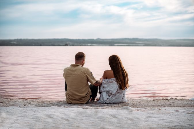 adorable couple sitting on an amazing beach with pink water