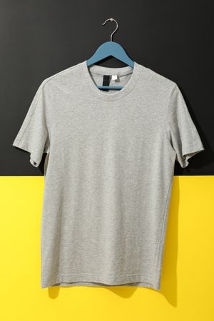 Hanger with blank gray t-shirt on two tone background, space for text