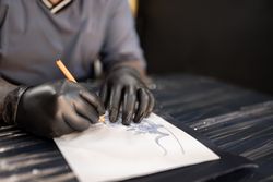 A tattoo artist is drawing a design stencil on his work stretcher before tattooing