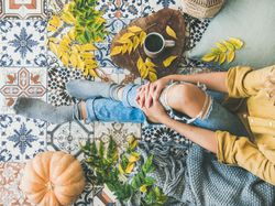 Woman sitting on colorfully tiled balcony with fall leaves and mug