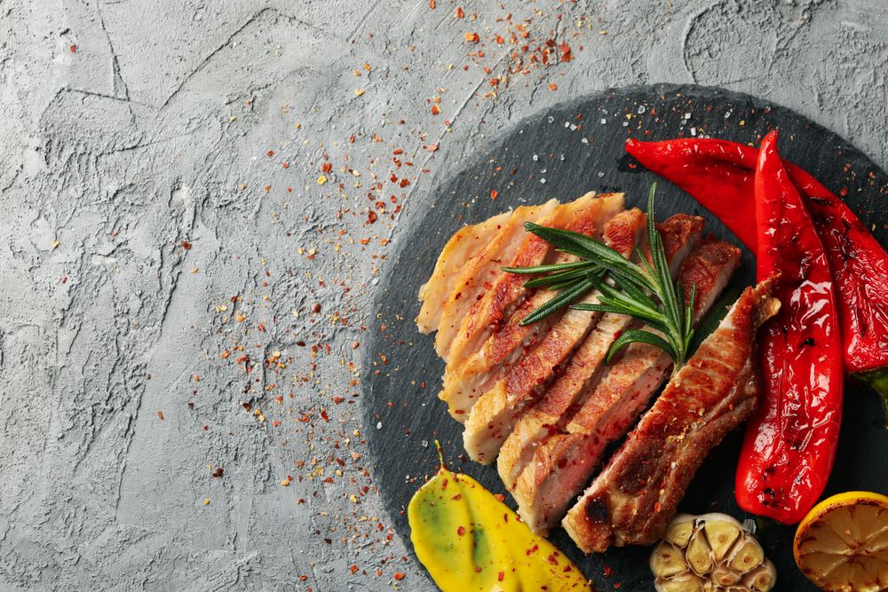 Tray with chopped pork steak and vegetables on gray background. Grilled food
