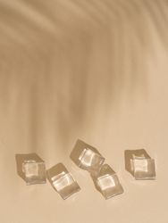 Flat lay of ice cubes on beige background with shadow of palm leaf