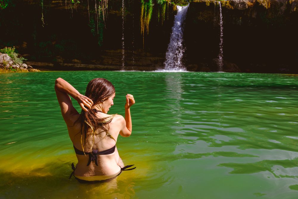 Anonymous woman touching hair and looking at waterfall