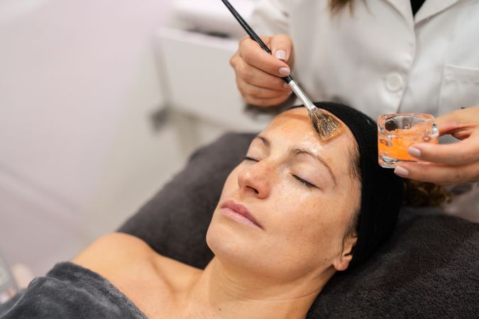 Cosmetologist brushing product on client's forehead