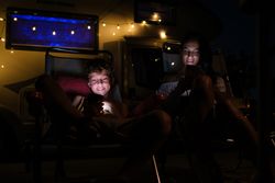 Mother and son using smartphones outside trailer at night