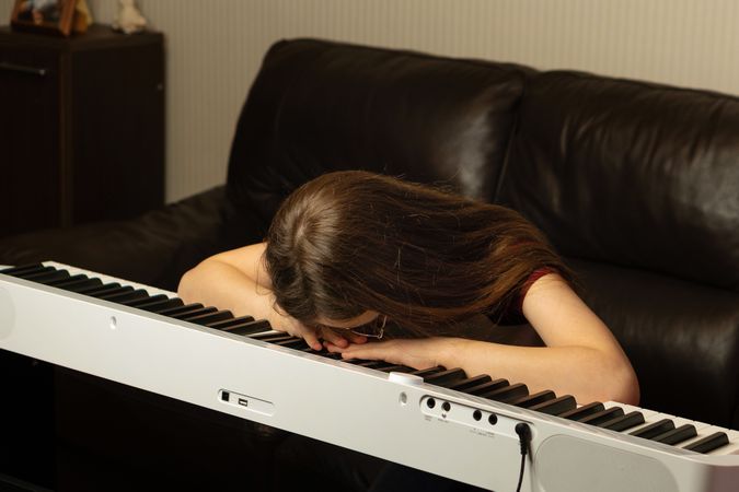 Girl with long hair resting head on piano keys