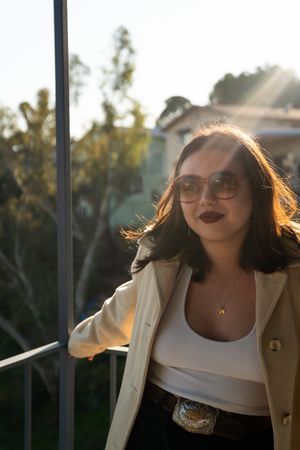 Young multiracial woman with sunglasses standing on patio with sun rays behind her