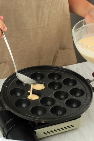 Hands spooning batter into bubble waffle maker for Japanese dish