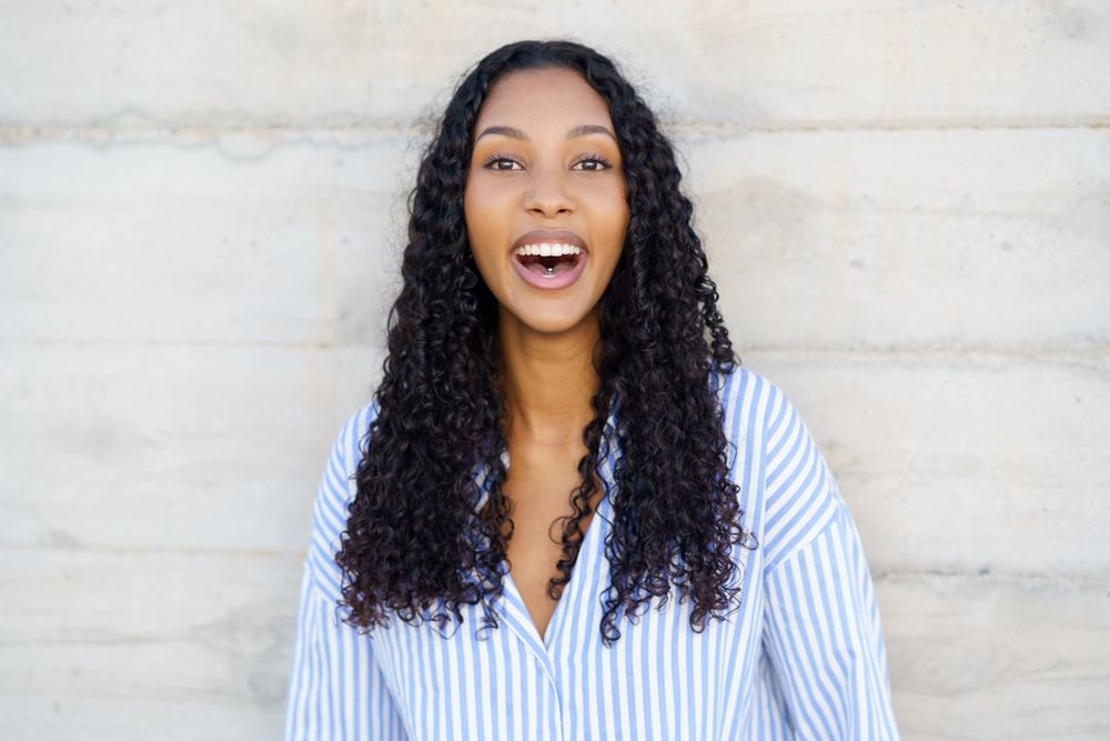 A Joyful Young Woman with Curly Hair Smiling Cheerfully Against a Neutral Background