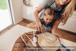 Cute girl sifting flour in bowl with her mother behind her 0LkDAb