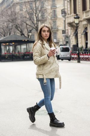 Portrait of woman walking in a European city street, with takeaway coffee in hands