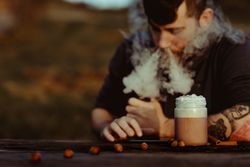 Vaper puffing smoke near a cup of fresh coffee