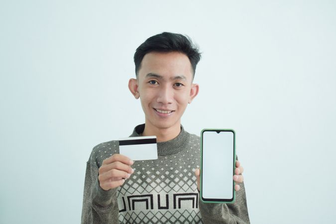 Smiling Asian businessman in suit holding blank credit card and smartphone