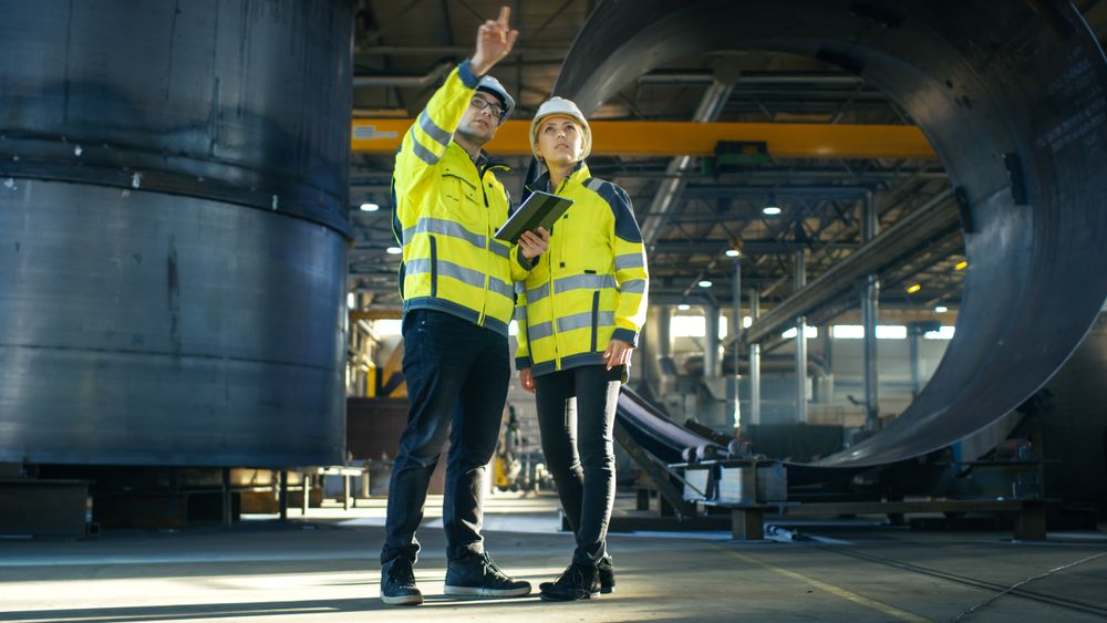 Male and Female Industrial Engineers in Hard Hats Discuss New Project while Using Tablet Computer.
