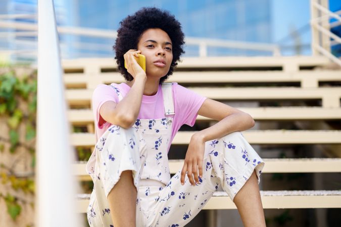 Woman in floral overalls sitting on stairs taking phone call