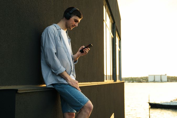Young man in headphones listen music against wall