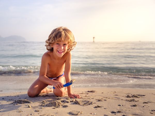 Smiling boy playing with toy shovel on sandy beach
