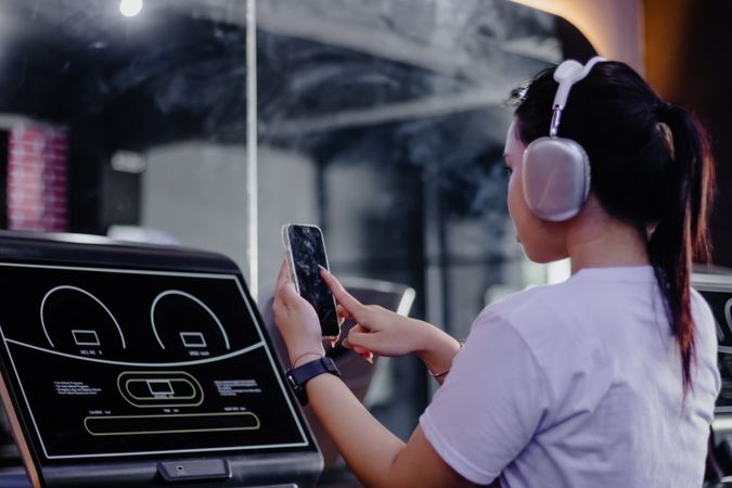 Young Woman Interacting with Phone on Treadmill at the Fitness C