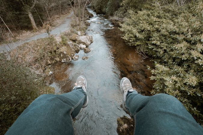 Tourist sitting on bridge and dangling legs over river