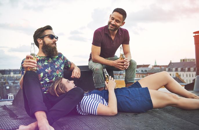 Three friends lounging on a roof with beer