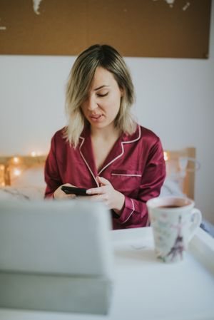 Woman sitting in bed with tablet and looking on smartphone